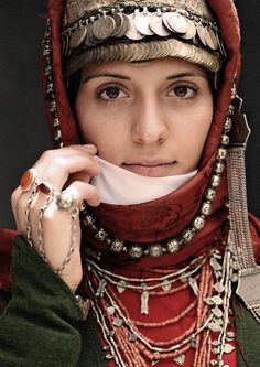 a woman wearing a red scarf and headdress with jewelry on her neck is posing for the camera