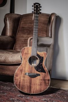 an acoustic guitar sitting on top of a rug in front of a brown leather chair