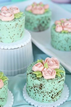 four cakes with frosting and flowers on them are sitting on a table next to plates