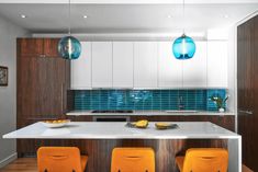 two orange chairs sit at the center of a kitchen island with white countertops and blue glass tile backsplash