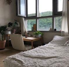 a bedroom with a bed, desk and large window overlooking the trees in the distance