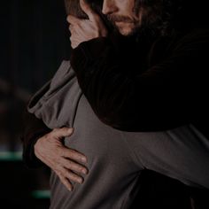 a man with long hair hugging another man in the dark