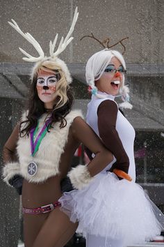 two women dressed up in costumes standing next to each other on a snow covered street