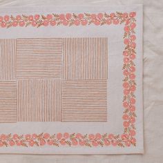 a piece of cloth with pink flowers and lines on the border, sitting on top of a white tablecloth