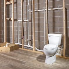 a white toilet sitting in a bathroom next to a brick wall with pipes on it