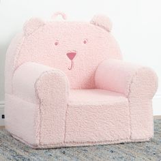 a pink teddy bear chair sitting on top of a carpeted floor next to a wall