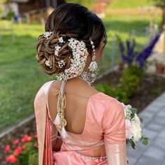 the back of a woman's head with flowers in her hair and jewelry on