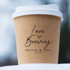 a cup of coffee with the words love is brewing written on it and a white lid