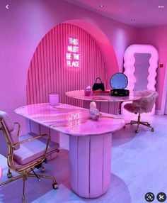 a pink room with chairs, desks and mirrors on the walls is lit by neon lights