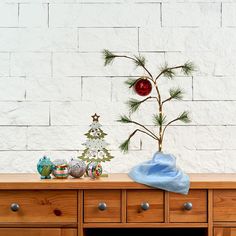 a wooden dresser with ornaments on it and a christmas tree in the corner, against a white brick wall