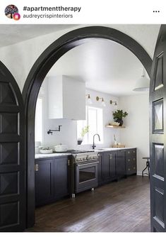 an arched doorway leads into a kitchen with dark wood floors and white walls, along with black cabinetry