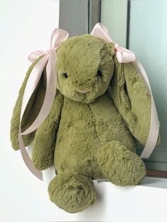 a green stuffed rabbit sitting on top of a window sill with a pink ribbon