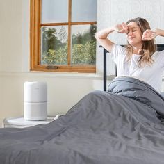 a woman sitting on top of a bed next to an air purifier