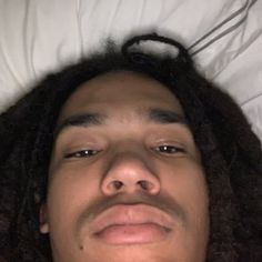 a man with dreadlocks laying in bed looking up at the camera and smiling