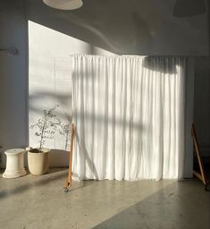 an empty room with white curtains and potted plants