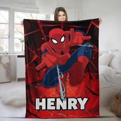 a woman holding up a spiderman blanket with the name henry on it in front of her