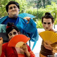 three people dressed in costumes holding fans