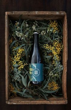 a bottle of beer in a wooden box surrounded by yellow flowers and greenery on a dark wood background