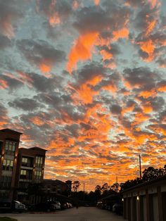 an orange and pink sky with some clouds in the background at sunset or dawn over a parking lot