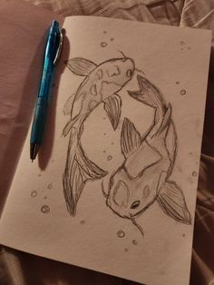 a drawing of two fish in a circle on paper with a pen next to it