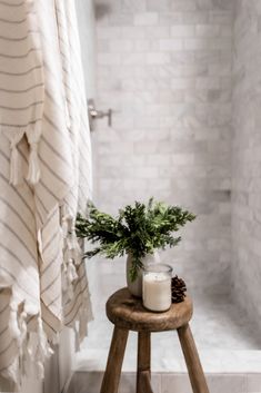 a wooden stool with a candle on it in front of a bathtub and shower curtain