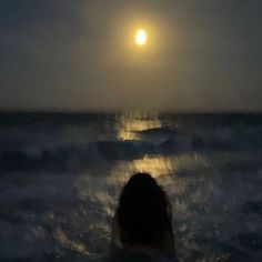 a woman standing in the ocean at night with her back turned to the camera and full moon behind her