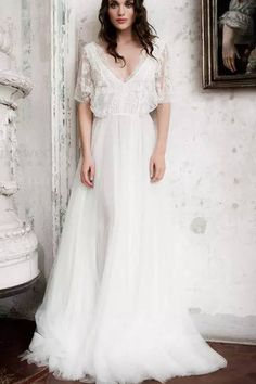 a woman standing in front of a wall wearing a white dress