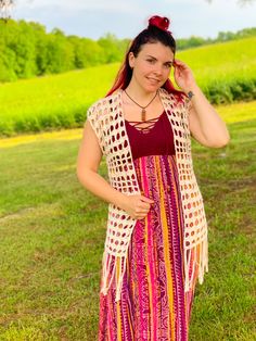 a woman standing in the grass with her hand on her head and wearing a colorful dress