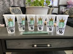 six starbucks cups with the number 16 on them are sitting on a table in front of a potted plant