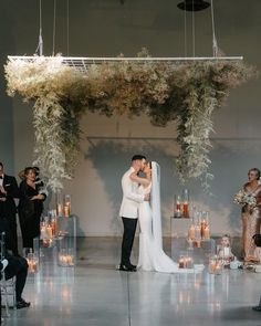 a bride and groom kissing in front of an altar with candles, flowers and greenery