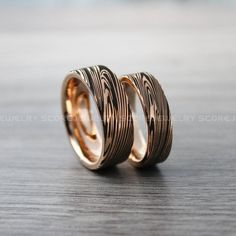 two gold wedding rings sitting on top of a wooden table with black and white stripes