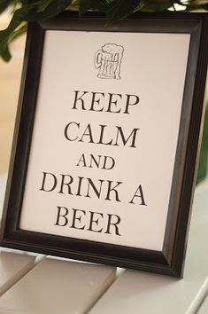 a framed sign that says keep calm and drink a beer on a table with flowers