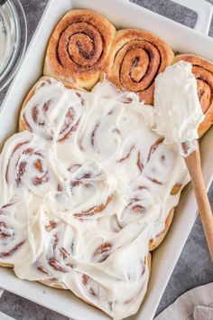 cinnamon rolls with cream cheese frosting in a white baking dish on a gray surface