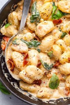 a skillet filled with shrimp and spinach covered in white sauce, garnished with basil