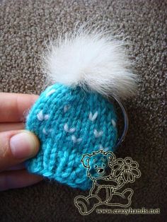 a hand holding a knitted keychain with a white pom - pom on it