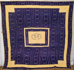 a purple and yellow quilt with two intertwined hearts on the center, in front of a white wall