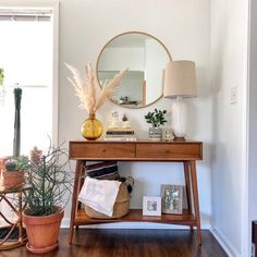 a wooden table topped with books and plants next to a wall mounted mirror on the wall