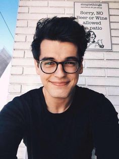 a man wearing glasses sitting in front of a brick wall