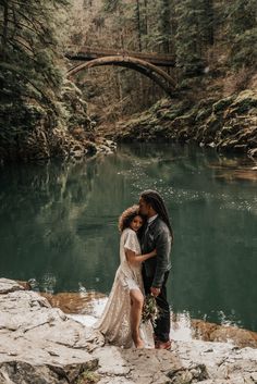 a man and woman standing next to each other in front of a river surrounded by trees