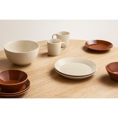 a wooden table topped with white and brown dinnerware on top of a wooden table