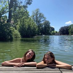 two women are laying on the dock in front of the water and smiling at the camera