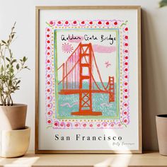 the san francisco golden gate bridge art print is displayed on a shelf next to a potted plant