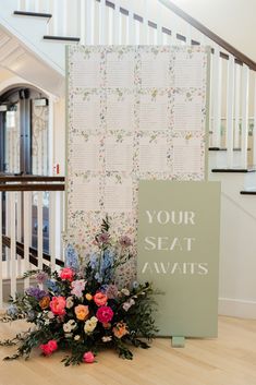 a floral arrangement on the floor next to a wedding seating chart and flower arrangement in front of a staircase