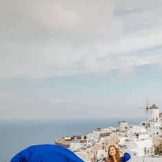 a woman standing next to a blue tent on top of a hill near the ocean