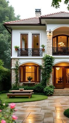 a large white house with lots of windows and plants on the front porch, surrounded by greenery