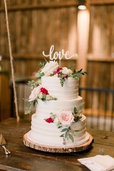 a white wedding cake with flowers and love written on the top is sitting on a wooden table