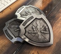 two metal shield badges sitting on top of a wooden table next to a computer keyboard