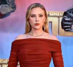 a woman in a red off the shoulder dress posing for a photo at an event