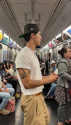 a man with tattoos on his arm standing in a subway car next to other people