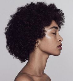 a woman with her eyes closed wearing gold hoop earrings on her left ear and black curly hair